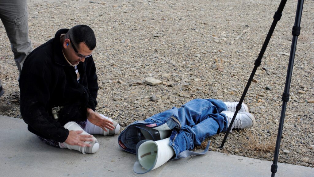 Double amputee above-the-knee sitting on the ground with detached prosthetic legs in blue jeans beside him.